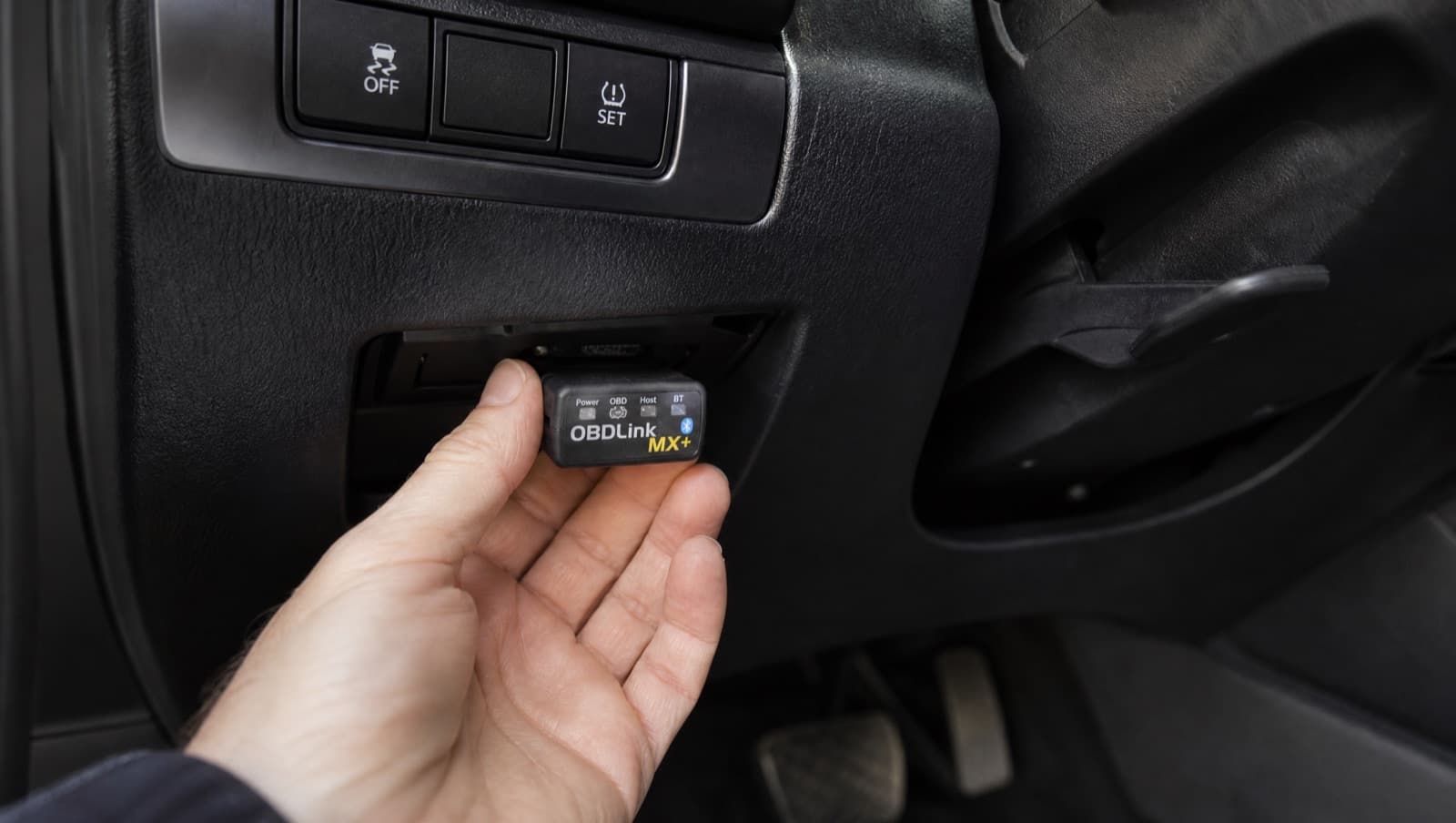 Plugging a Bluetooth OBD-II adapter into the port under a car dashboard